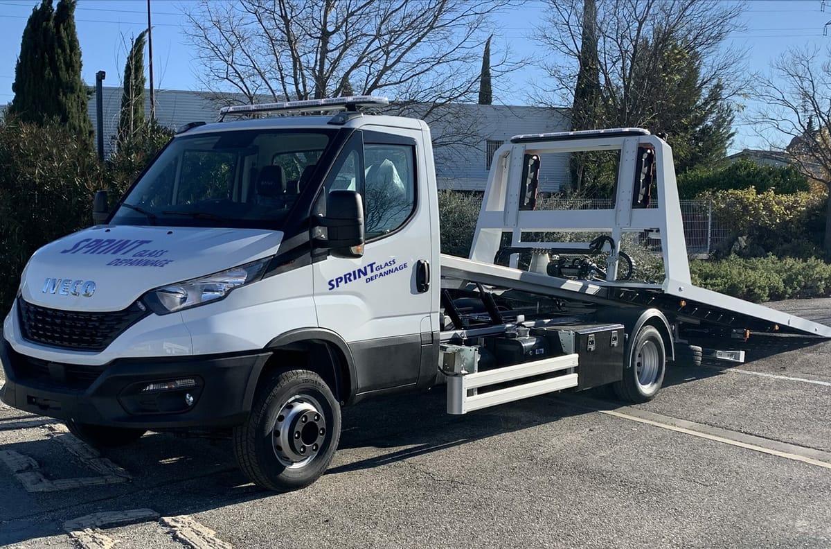 La dépanneuse plateau Iveco Daily blanche aux couleurs de Sprint Glass Dépannage, garée sur un parking